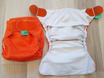 Kaksi oranssia Tots Bots taskuvaippaa. Oikeanpuoleinen ylhäältä kuvattu, vasemmanpuoleinen avattu tasolle sisäpuoli ylöspäin.