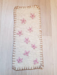Suorakaiteen muotoinen villaimu, johon neulottu vaaleanpunaisia kukkia ja tikkaukset reunoille.
