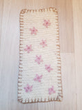 Suorakaiteen muotoinen villaimu, johon neulottu vaaleanpunaisia kukkia ja tikkaukset reunoille.